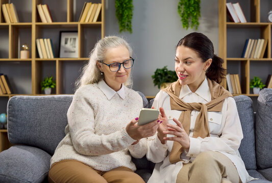 Senior woman with caregiver and consultant using smartphone. They discuss finance and retirement, with daughter sharing advice and assistance for apps. Clear concept of tech help at home.
