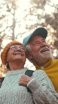Headshot of a happy senior couple embracing and looking up with joyful smiles while hiking in the woods. Mature people enjoying active retirement and healthy outdoor leisure activity