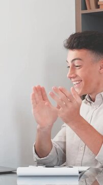 Successful young businessman feeling happy and excited after reading good news on his laptop, celebrating a business achievement with clenched fists while working at his modern home office desk