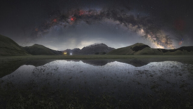 View of the Milky Way galaxy arching over the mountains and reflecting in a pool of water in the plains of Castelluccio, Umbria, Italy.