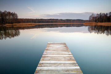 Obraz premium Wooden pier leading into a calm lake with perfect reflections at sunrise