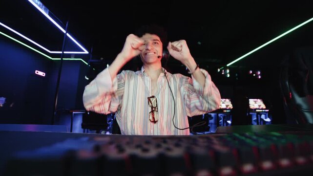 Young curly-haired gamer playing a computer video game in a neon-lit gaming club.