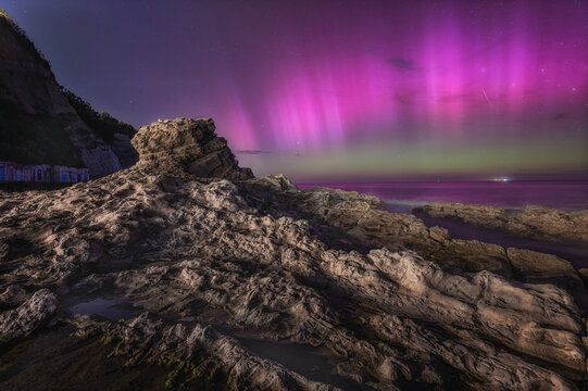 View of the Seggiola del Papa rock formation illuminated by the aurora borealis at night along the coast in Ancona, Marche, Italy.