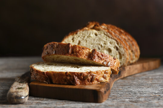 Bread Still Life. A loaf of sliced multi grain bread on a cutting board on a rustic wood table and a mottled brown backgorund.