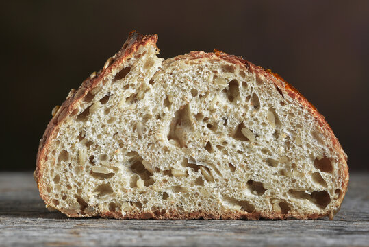 Bread Still Life. Closeup of a single slice of multi grain bread on a rustic wood table and a mottled brown backgorund.