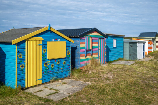 Brightly painted colorful wooden beach huts stand in a row along the grassy coastline of Hopeman in Moray Scotland during a clear day