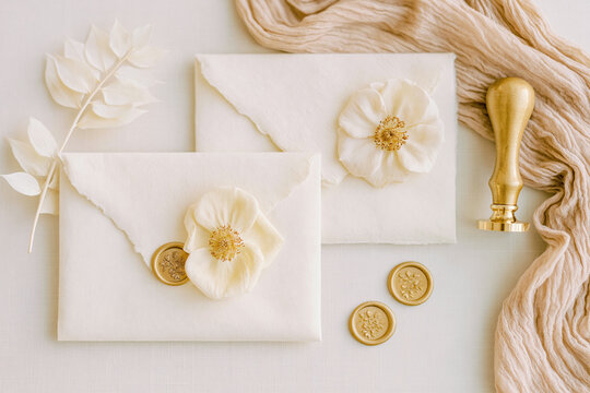 Elegant wedding stationery arranged with handmade paper envelopes, white flowers, botanical details, and gold wax seals