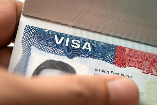 United States visa stamp inside an open passport document, held by a hand, for immigration, international travel, border security, visa application, and citizenship topics.