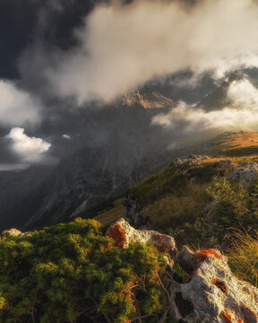 View of the dramatic mountain landscape with rocky outcrops, lush vegetation, and golden sunlight breaking through storm clouds in Prati di Tivo, Abruzzo, Italy.