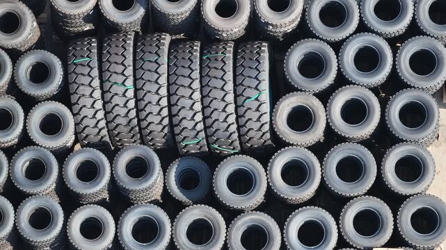 Large stacks of black heavy-duty vehicle tires organized in a spacious outdoor industrial warehouse