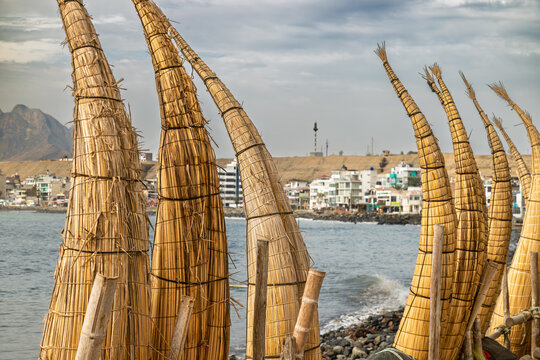 Traditional reed boats standing on rocky shore of Huanchaco beach with coastal town and Pacific Ocean in background
