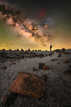 View of a person standing on the volcanic terrain of Minas de San Jose under the bright Milky Way galaxy at night in La Orotava, Canary Islands, Spain.