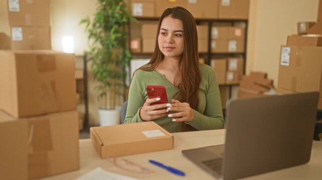 Woman holding phone and stacking parcel boxes in a small business building; determination entrepreneurship.