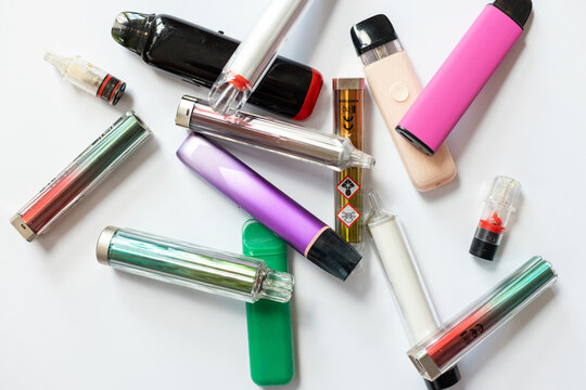 A pile of colorful disposable e-cigarettes with toxic warning symbols, representing nicotine addiction, chemical hazards, and the health risks of modern electronic vaping devices.