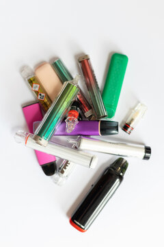 A piled heap of colorful disposable vapes and pods with toxic warning symbols, demonstrating nicotine addiction, health hazards, and chemical risks of e-cigarettes on a white background.