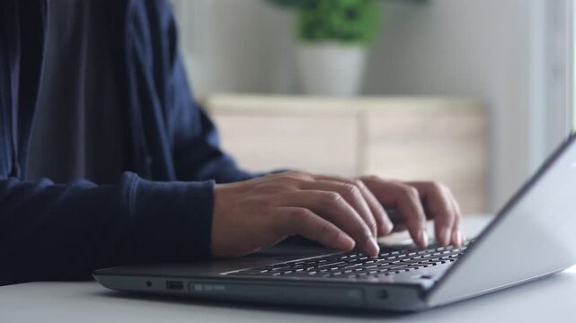 A man's hand is typing on a laptop computer keyboard at home or in the office. He is working, sending messages, chatting, browsing the internet, and using social networking.