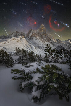 View of Passo Rolle at night with a meteor shower illuminating the snow-covered peaks, pine trees, and winter landscape in Passo Rolle, Trentino-Alto Adige, Italy.