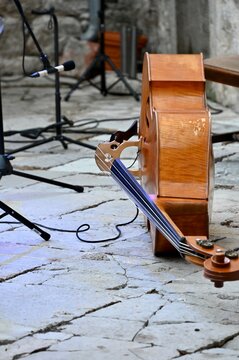 A close-up side view of a double bass standing upright on an old stone paved floor during an outdoor music performance setup.