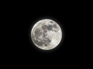 Fototapeta premium A full moon isolated against a pitch-black background showing detailed surface craters and lunar terrain.