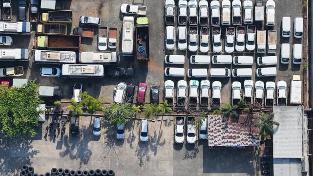 Many white trucks parked in rows inside a large open outdoor facility during the day