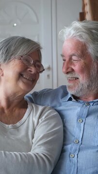 Portrait of a happy, beautiful senior couple laughing while looking at each other, enjoying their retirement together at home, expressing love, tenderness, and complicity