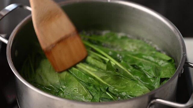 Blanching fresh green spinach in a pot of boiling water and stirring with wooden spatula, preparing ingredients for Korean spinach salad (Sigeumchi namul)