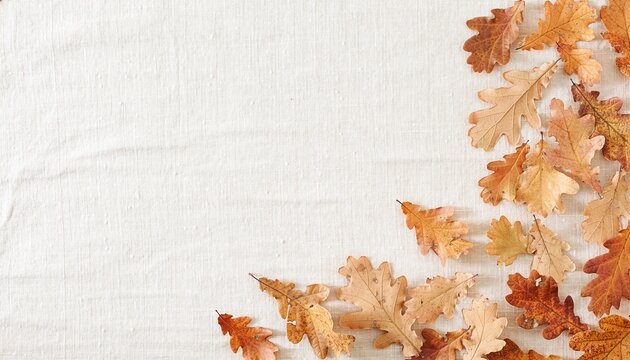 Top view of dry brown autumn oak leaves arranged as a border on a rustic light linen fabric background. Minimalist flat lay composition with ample copy space for seasonal design.