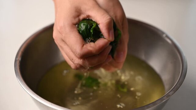 Hands squeezing excess water out of blanched spinach before seasoning, preparing for Korean spinach salad (Sigeumchi namul)