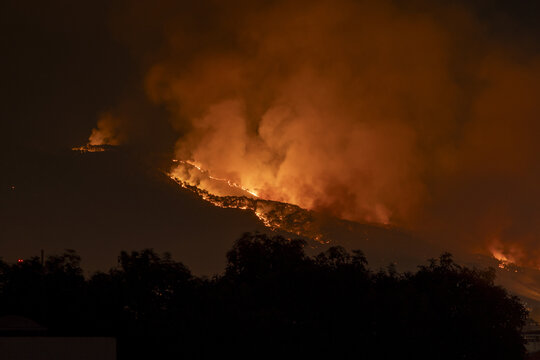 View of a large wildfire burning on a hillside at night, with bright orange flames and thick smoke rising into the dark sky in Uruapan, Michoacan, Mexico.