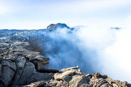 View of Erta Ale volcanic crater with solidified lava rock and rising steam.