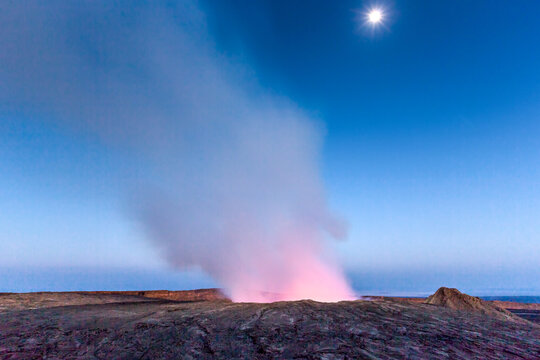 View of the active lava lake at Erta Ale volcano with glowing smoke rising into the twilight sky, Ethiopia.