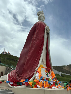 View of the Princess Wencheng statue draped in a red cloak with colorful prayer flags at the base, set against a grassy mountain landscape in Xining, Qinghai, China.