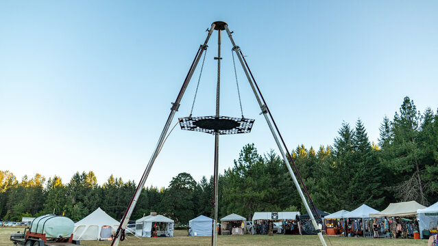 View of the Oregon Country Fair featuring a large tripod structure with a suspended platform, surrounded by vendor tents and a forest in Veneta, Oregon, United States.