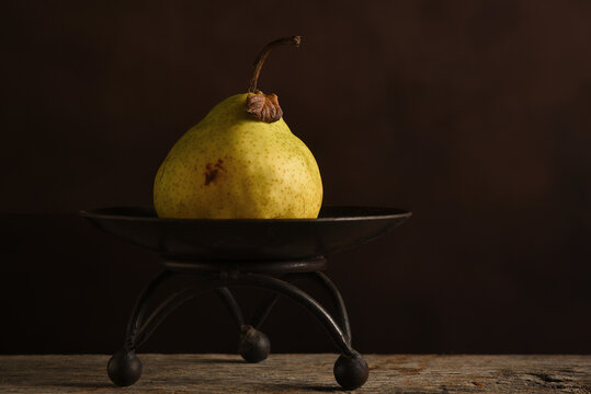 Fruit Still Life. An Anjou Pear on a pedestal against a warm brown mottled background.