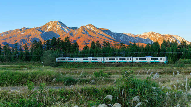 山肌だけが朝日を浴びて真っ赤に染まった瞬間にえちごトキめき鉄道が静かに田園を走り抜ける