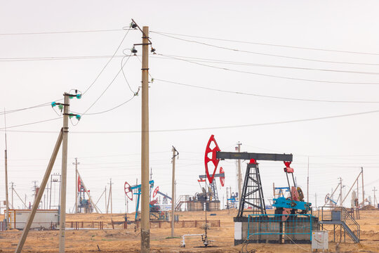 View of oil field pumpjacks operating in the arid landscape with power lines and industrial equipment in Zhanaozen, Mangystau Region, Kazakhstan.
