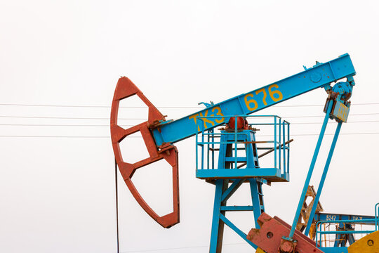 View of a blue industrial oil pumpjack with a red counterweight operating in an oil field in Zhanaozen, Mangystau Region, Kazakhstan.