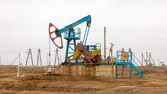 View of an oil pump jack operating in an oil field with power lines and flat desert terrain in the background in Zhanaozen, Mangystau Region, Kazakhstan.