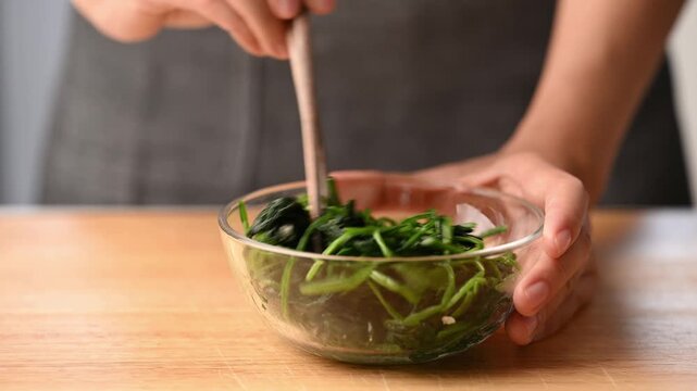 Woman hands using chopsticks to mix Korean spinach salad (Sigeumchi namul) in a bowl