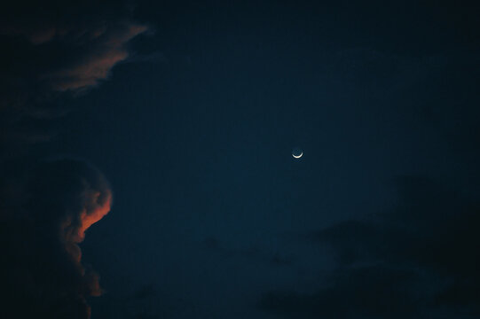 View of a crescent moon shining in the dark night sky with soft clouds in Guatemala.