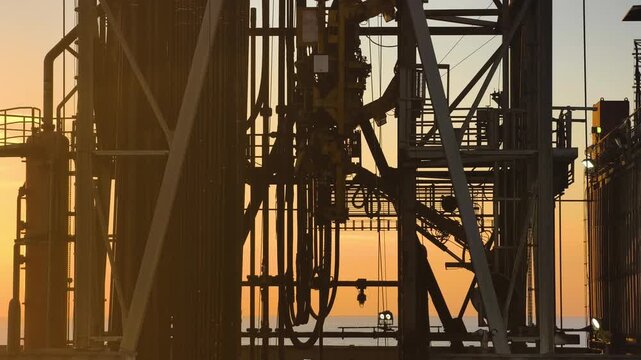Top Drive System (TDS) in the derrick, offshore Jack-Up Rig Mast Structure during sunset time in the middle of the ocean