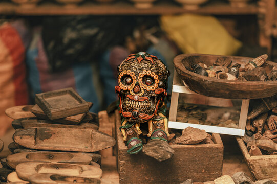 View of a decorative calavera skull surrounded by wooden weaving shuttles and a bowl of small tokens in a market stall in Antigua Guatemala, Sacatepequez Department, Guatemala.