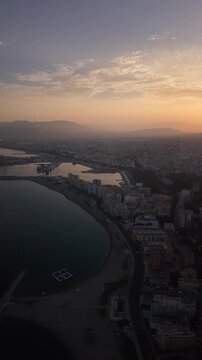 Aerial view of Malaga bullring (Plaza de Toros de la Malagueta) illuminated at sunset. Cinematic drone shot of the coastal arena, Mediterranean sea, and city skyline during golden hour.