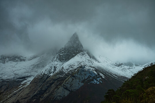 View of the iconic Stetind mountain peak partially obscured by heavy clouds with snow-covered slopes and rocky terrain in Narvik Municipality, Nordland, Norway.