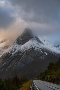 View of the snow-covered Stetind mountain peak partially obscured by clouds above a road in Narvik Municipality, Nordland, Norway.