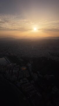 Aerial view of Malaga bullring (Plaza de Toros de la Malagueta) illuminated at sunset. Cinematic drone shot of the coastal arena, Mediterranean sea, and city skyline during golden hour.