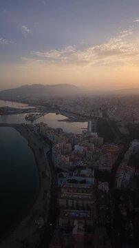 Aerial view of Malaga bullring (Plaza de Toros de la Malagueta) illuminated at sunset. Cinematic drone shot of the coastal arena, Mediterranean sea, and city skyline during golden hour.