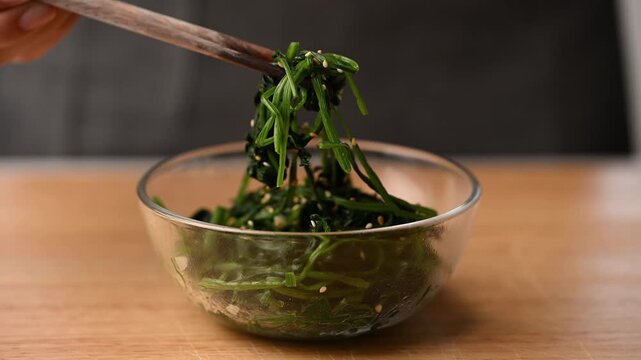 Hand using chopsticks to eating Korean spinach salad (Segeumchi namul) in a bowl
