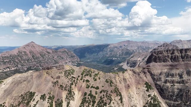 Aerial of Uinta Wasatch Cache National Forest mountain range in Utah with prominent exposed rock cliffs and deep canyons carved into the mountainsides under a dramatic sky in summer