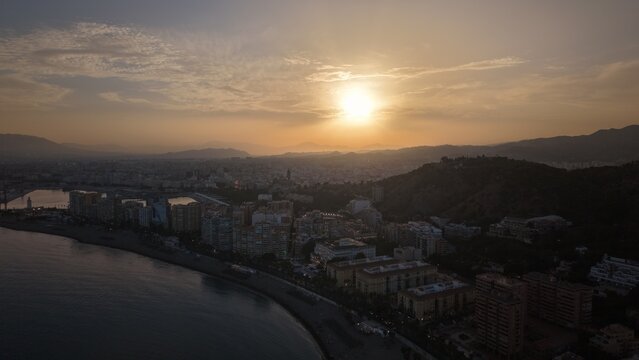Aerial view of Malaga bullring (Plaza de Toros de la Malagueta) illuminated at sunset. Cinematic drone shot of the coastal arena, Mediterranean sea, and city skyline during golden hour.